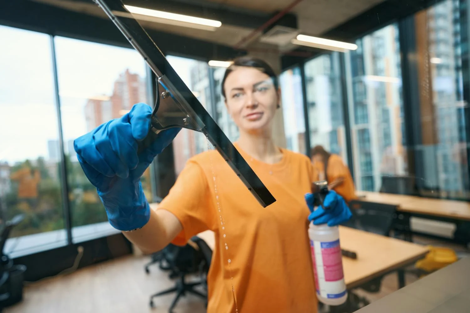 Reinigungskraft reinigt eine Glasfront in einem Büro mit Abzieher
