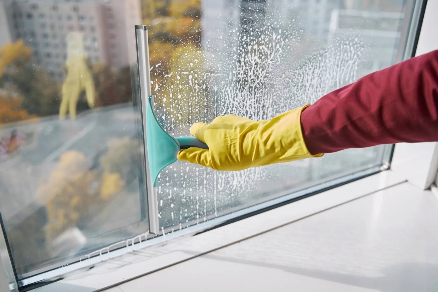 Fensterreiniger zieht mit einem Abzieher Seifenwasser von einer Glasscheibe ab